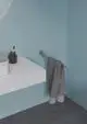 Handtuchstange aus Chrom an einer blauen Wand, gehalten von einem Wandhalter. In der Nähe befindet sich ein Waschbecken und ein Behälter von Ideal Standard.